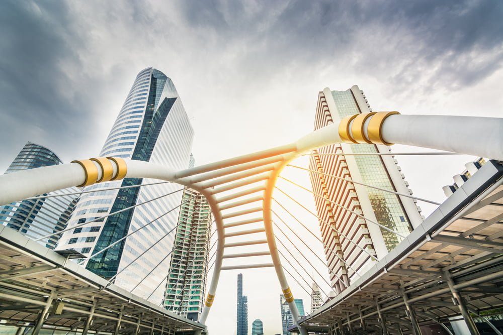 A scenic view of a bridge over Bangkok, framed by towering buildings that define the city's skyline.