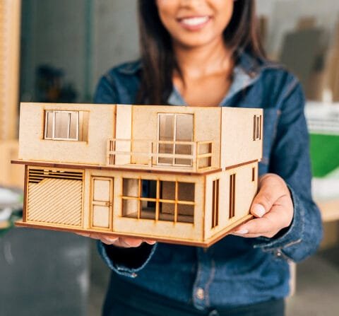 Woman holding a wooden architectural model with a blurred workshop background, symbolising Modular Construction Southeast Asia.