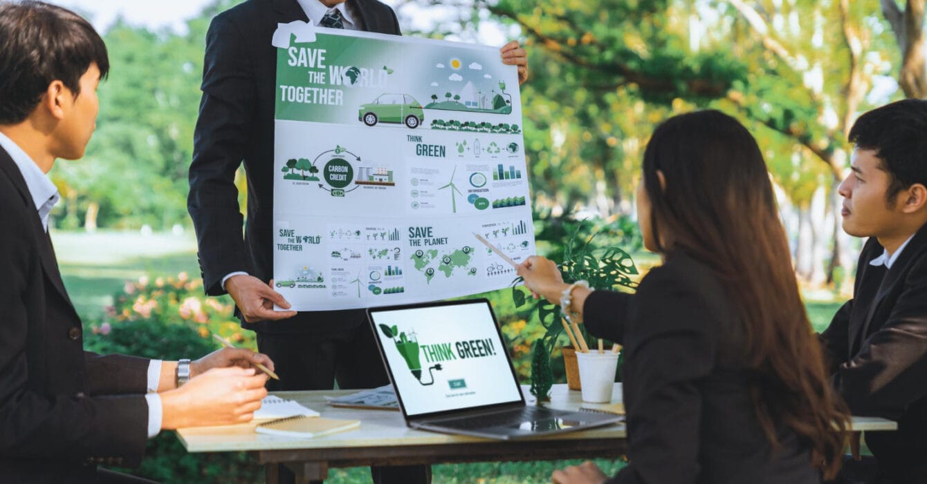 Four professionals discussing a "Save the World Together" environmental poster outdoors, symbolising the needs of Green Infrastructure Southeast Asia.