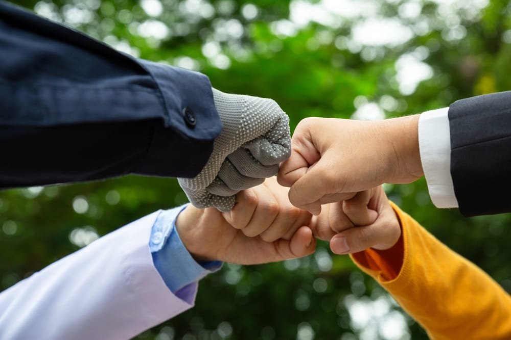 Four people making a fist bump gesture with a blurred green background, symbolising the collaboration between the government, the private sector and the public (Public-Private Partnerships Southeast Asia).