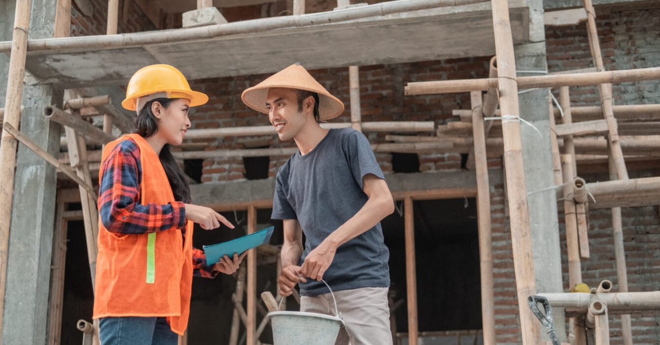 Skilled Workforce in Southeast Asia Construction: Two construction workers conversing at a building site with scaffolding in the background.