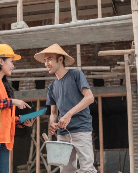 Skilled Workforce in Southeast Asia Construction: Two construction workers conversing at a building site with scaffolding in the background.