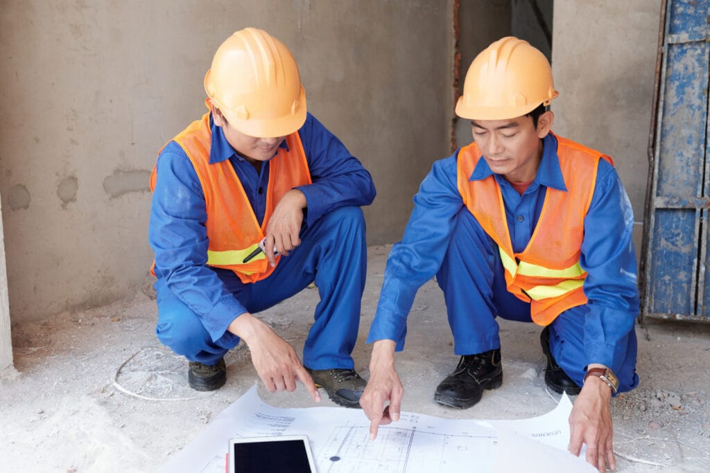 Two construction workers in safety gear examining blueprints at a worksite, symbolising Skilled Workforce in Southeast Asia Construction.