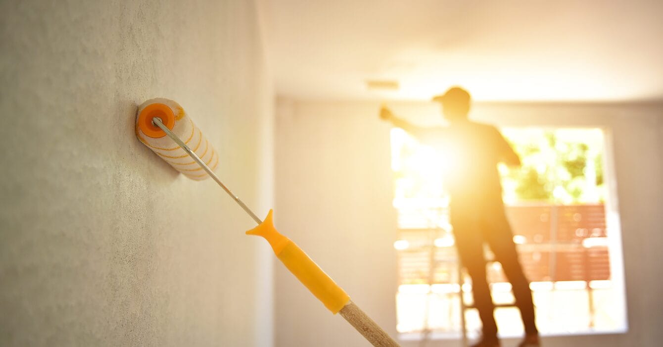 Southeast Asia’s Future Construction Market and paint roller on a wall with a blurred silhouette of a person painting in the background.