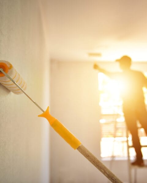 Southeast Asia’s Future Construction Market and paint roller on a wall with a blurred silhouette of a person painting in the background.